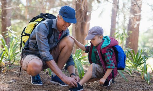 Mature father tying sports shoelace for son in forest