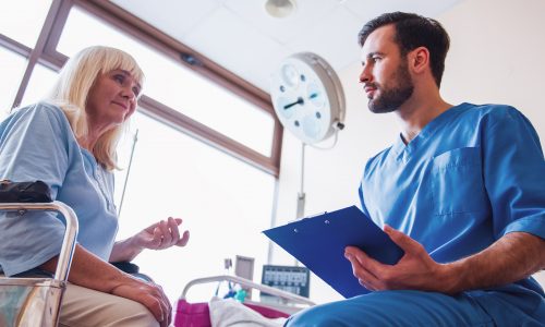 Beautiful old lady is talking to a handsome doctor while sitting in the wheelchair in hospital ward