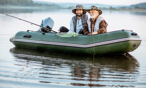 Portrait of a grandfather with adult son fishing on the inflatable boat on the lake early in the morning