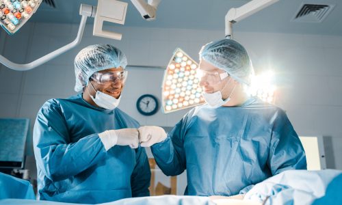 nurse and surgeon in uniforms doing gesture and smiling in operating room